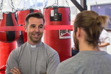 smiling young make in clergy shirt, in front of red punchbags