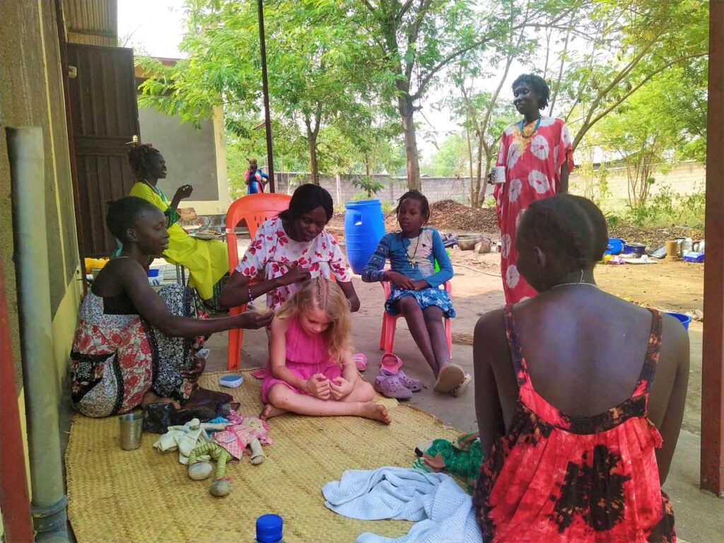 Women of Gambella sitting talking and braiding hair of Suzy's daughter