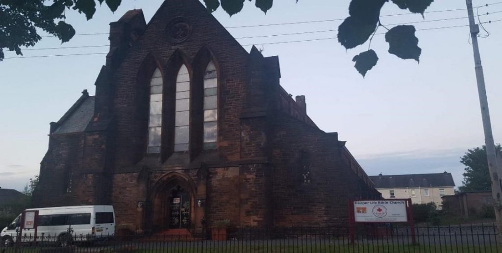 traditional church exterior with white minibus outside and signboard: "Deeper Life Bible Church"