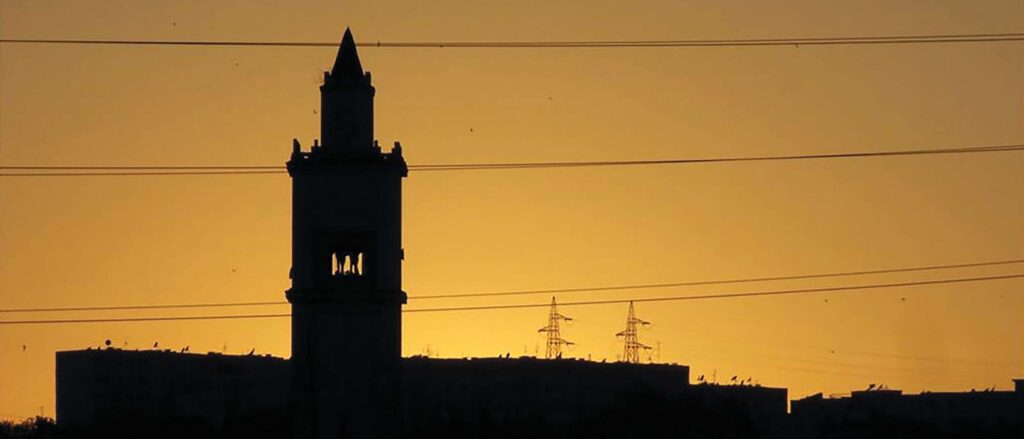 square towered mosque silhouetted against yellow sky