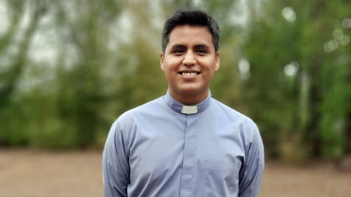 Smiling young Latino man in light grey clerical shirt