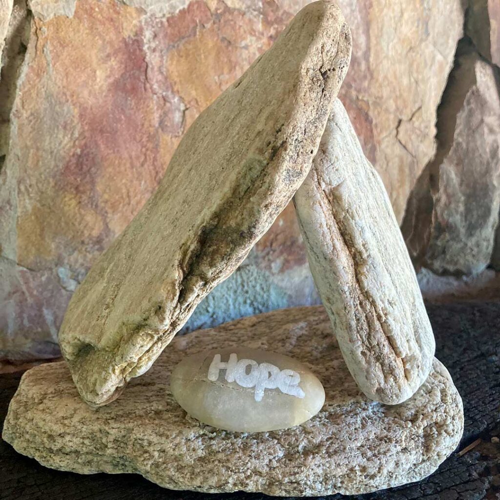 "hope" is painted on a smooth pebble, sheltered by fragments of rock in a prayer space
