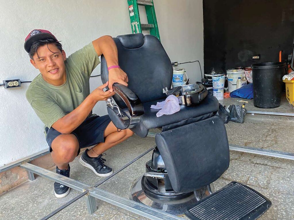 Young man crouches next to barber's chair among rags and tools