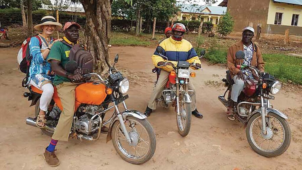 Three motorbikes in a dusty hospital compound, with two people on each, ready to roll