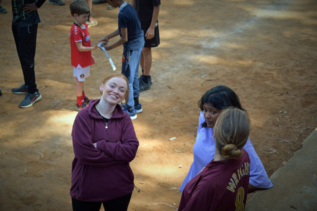 young female volunteer smiles with friends and pupils in school playground