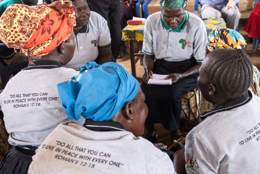 group of women discussing; they wear t-shirts with slogan "Do all that you can to live in peace with every one" Romans 12:18