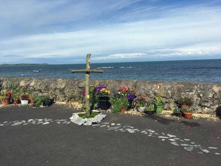 wooden cross with planted flower tubs next to sea wall