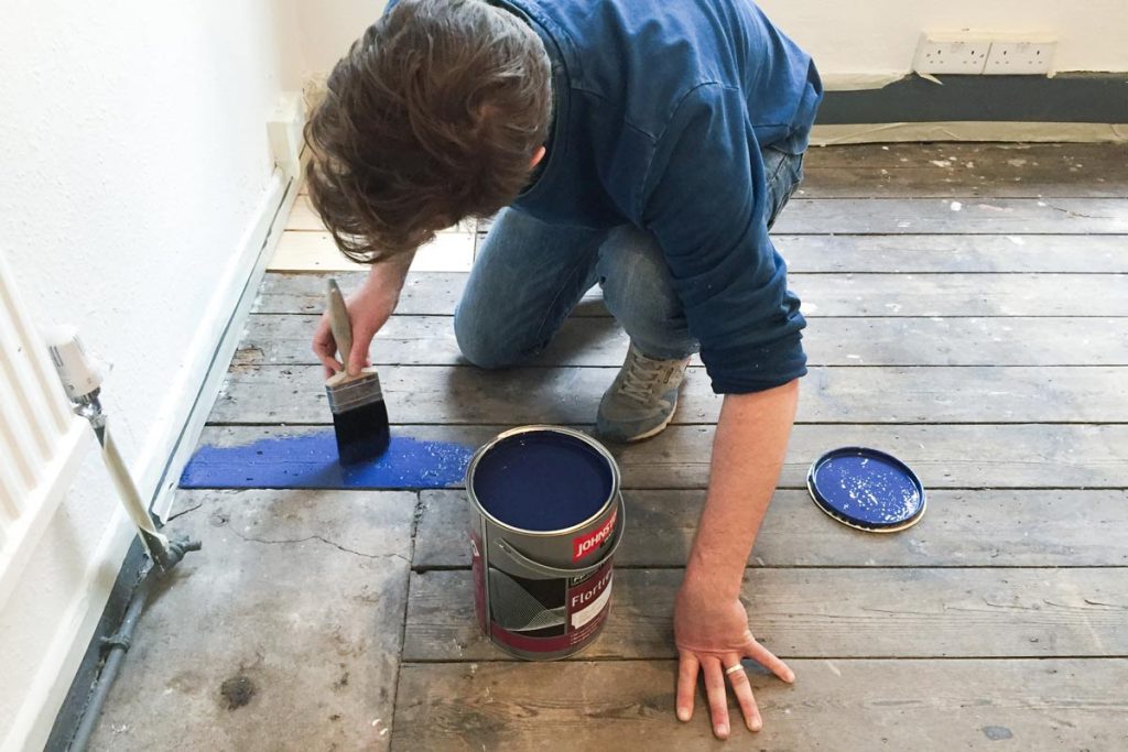 man paints floorboards a deep blue colour