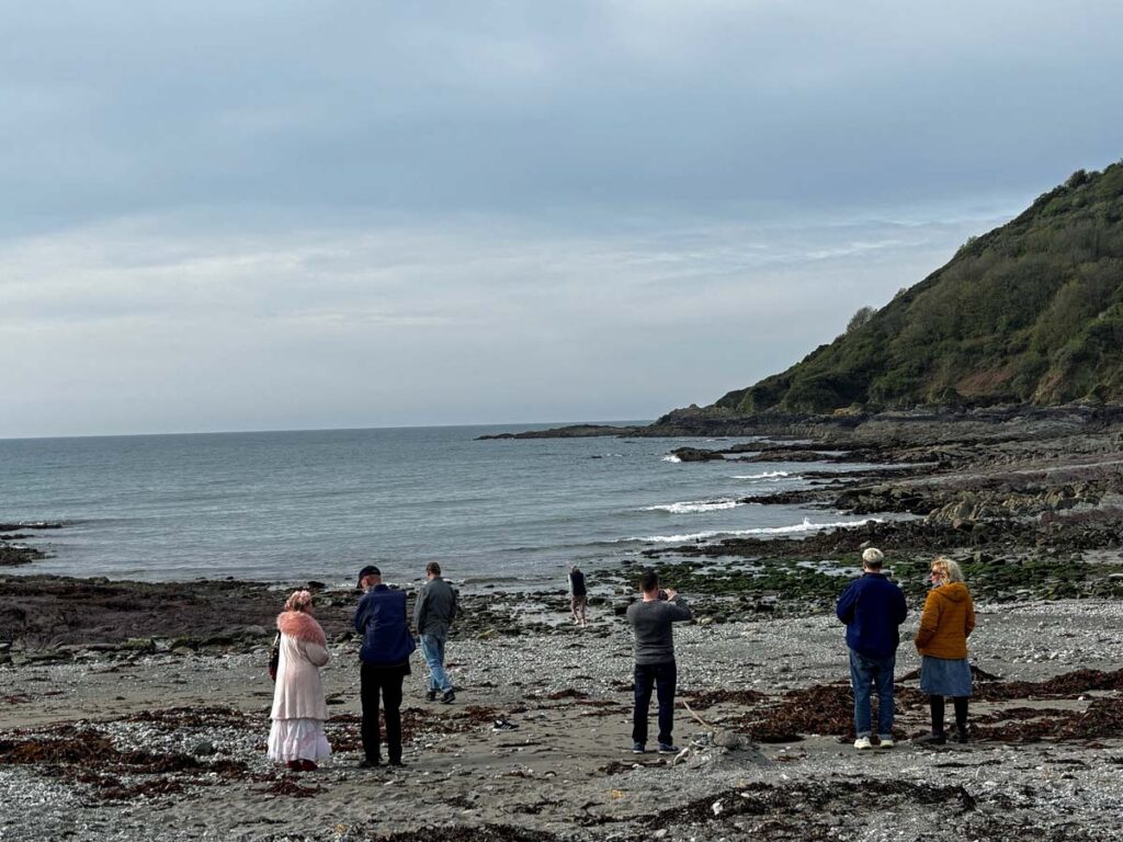 figures on pebble beach beneath a grey-blue sky
