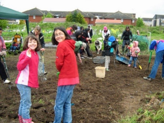 smiling children join in digging a patch of soil