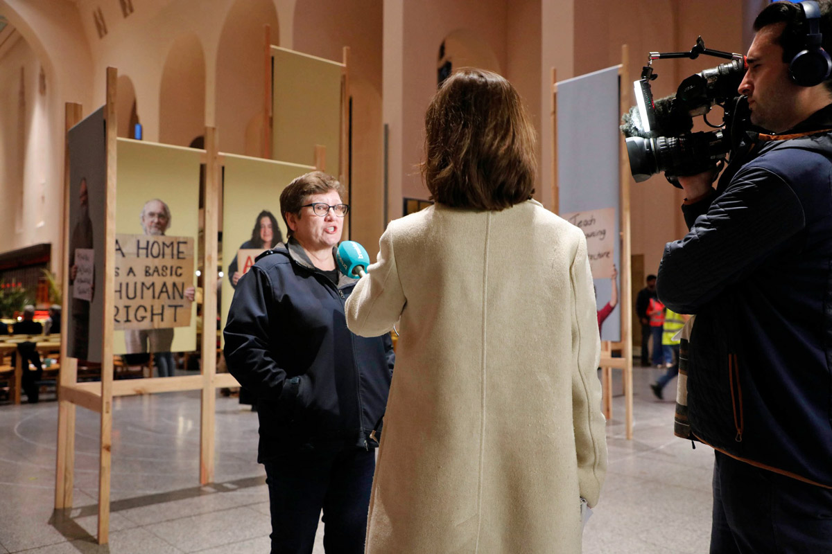 woman interviewed on camera in front of art exhibit