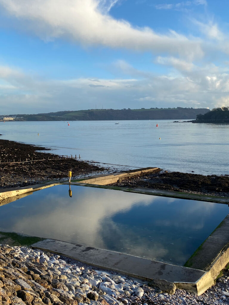 lone man stands on edge of beachside pool, reflecting the sky like a mirror