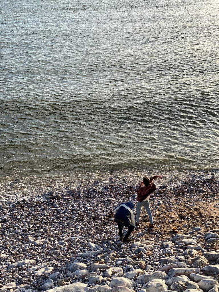 two youngsters on beach throwing pebbles into sea 