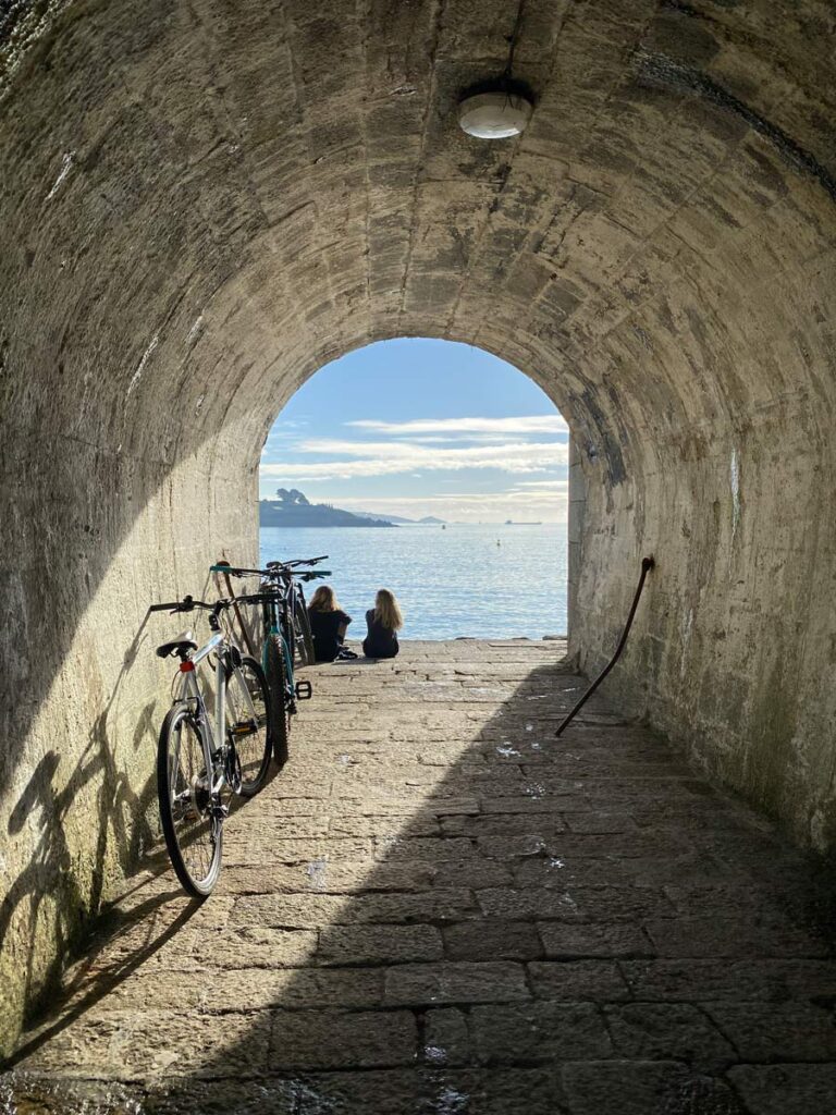 two women silhouetted in tunnel archway overlooking sea