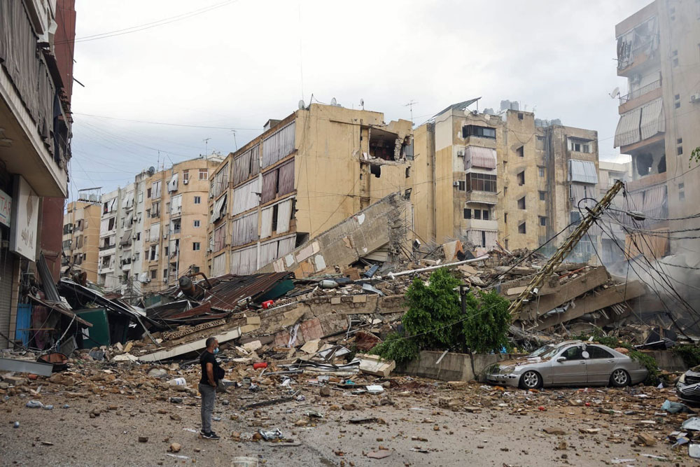 man stares at destroyed building that collapsed on car