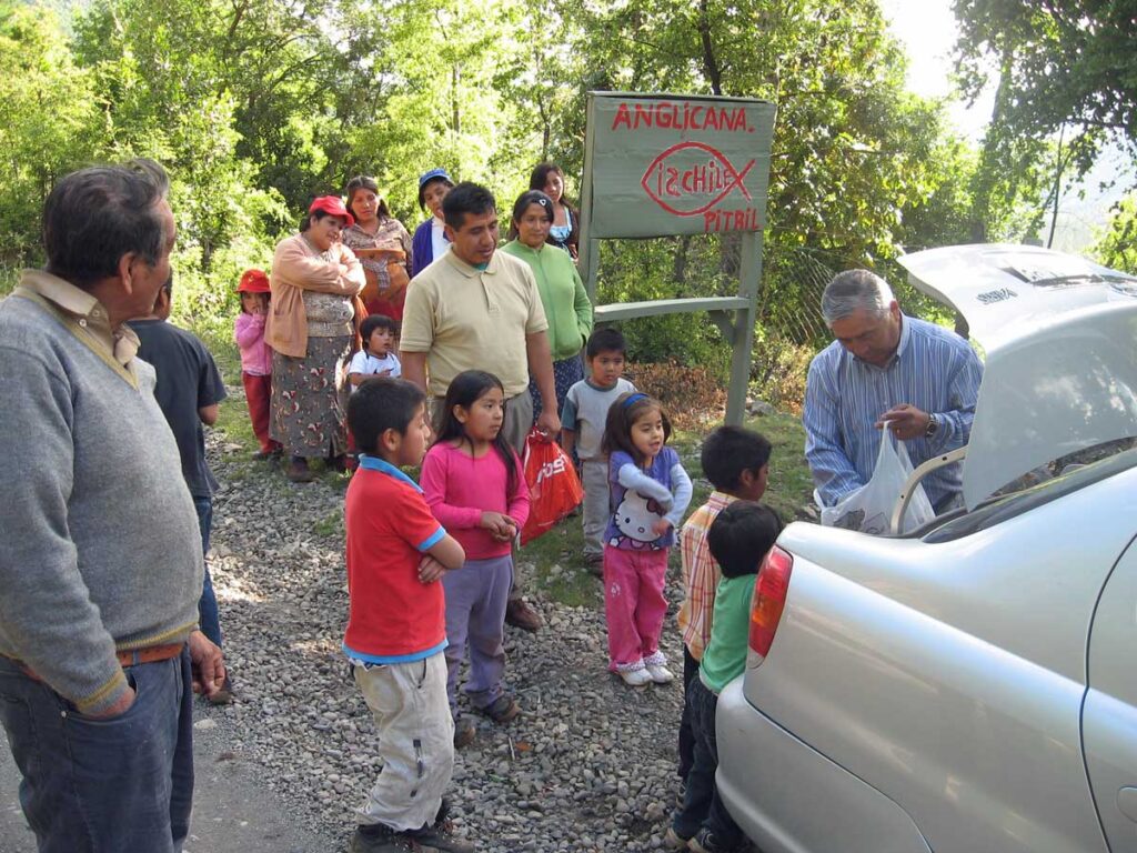 Bishop Abelino, in 'civilian' clothes, reaches into a carrier bag while children wait eagerly