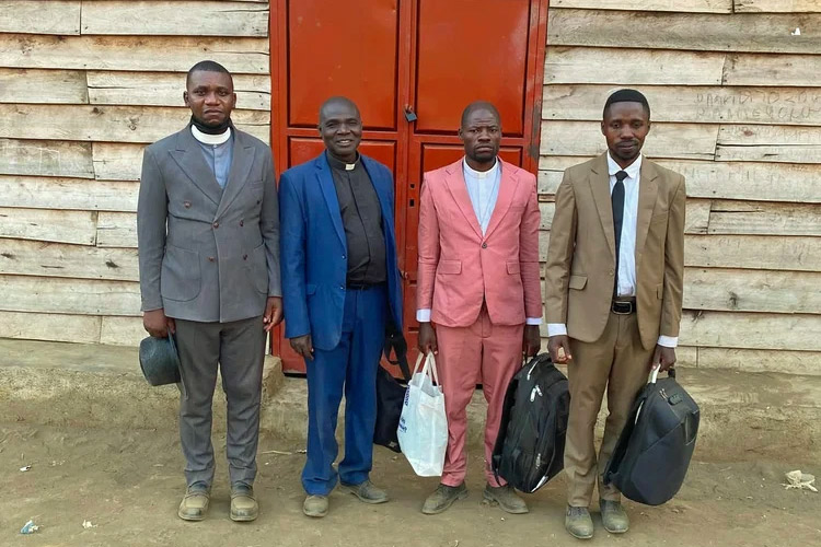 four Congolese clergy in front of red door in wooden slatted building