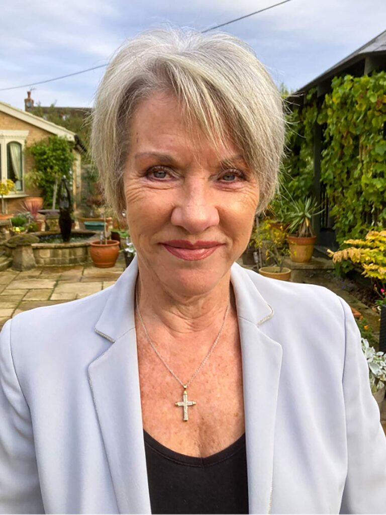 Jane smiles warmly, with silver hair and a cross necklace
