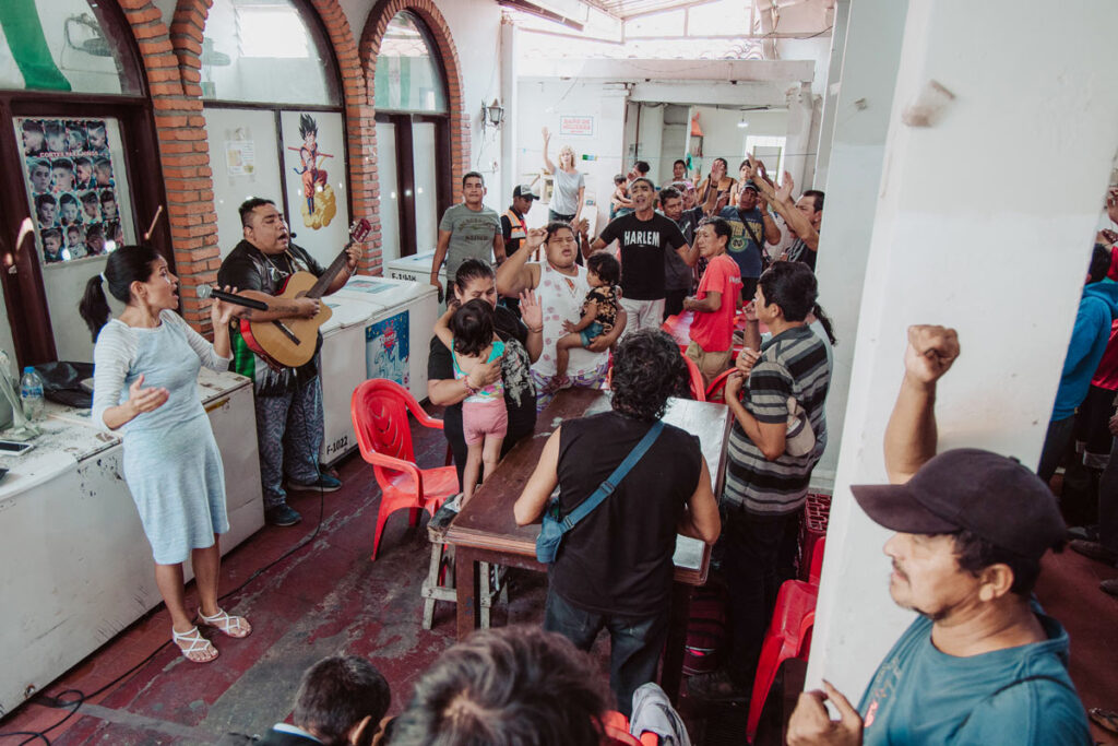 Guitarist, singer and several people with raised hands among a small crowd filling the toilet block premises