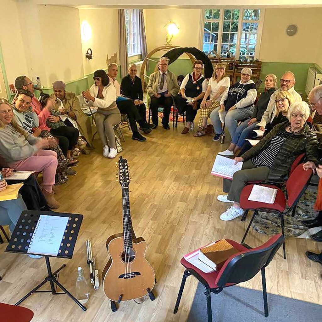 people seated informally in an oval, a guitar on a stand
